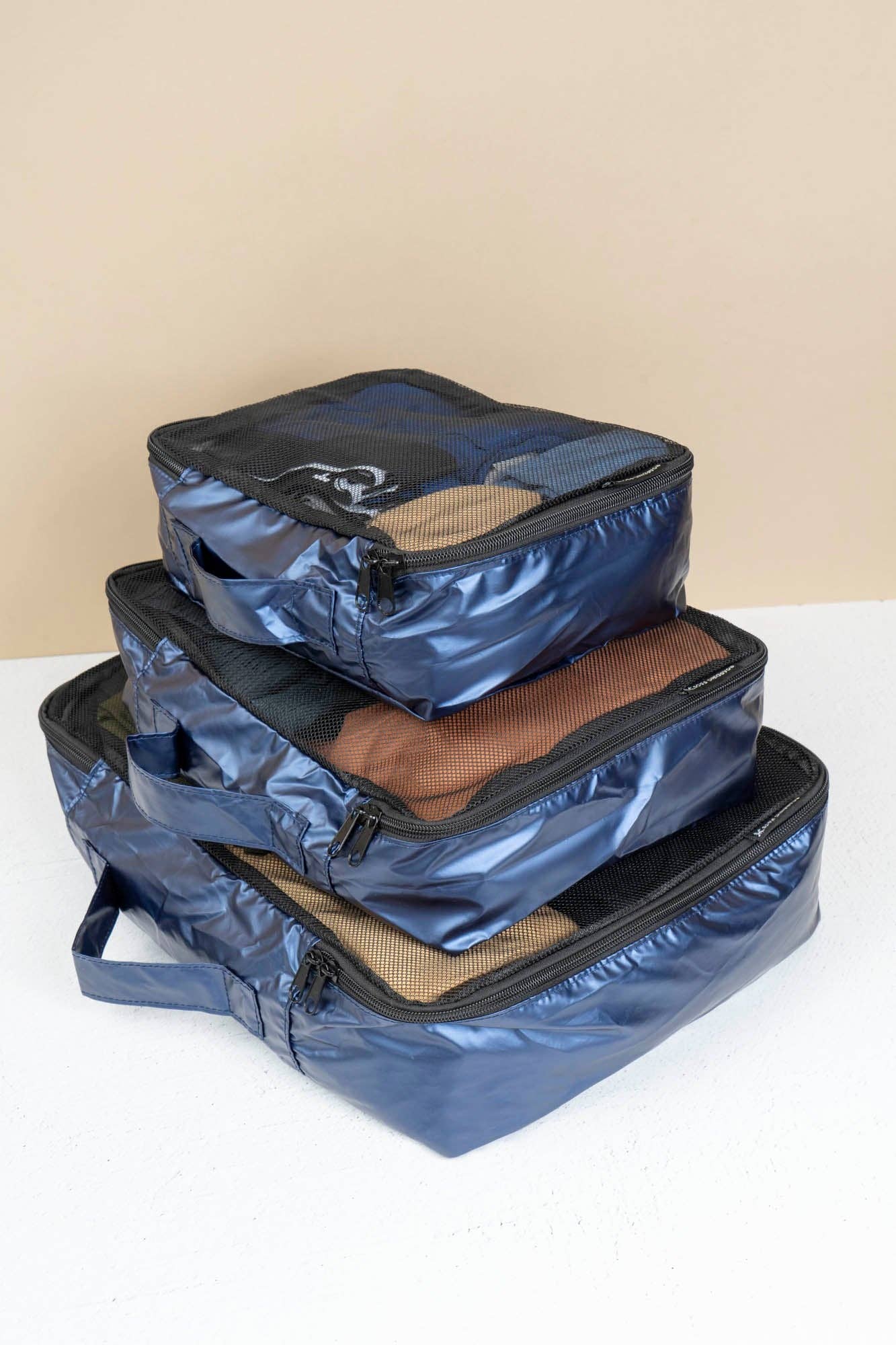 Three blue packing cubes stacked on a white surface with a beige background