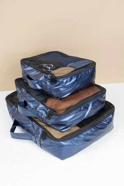 Three blue packing cubes stacked on a white surface with a beige background